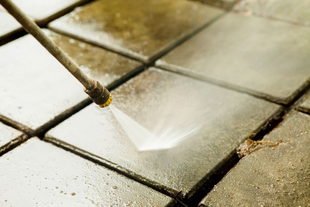 A Person is Using a High Pressure Washer to Clean a Tile Floor — Dynamic Services in Blackwater, QLD