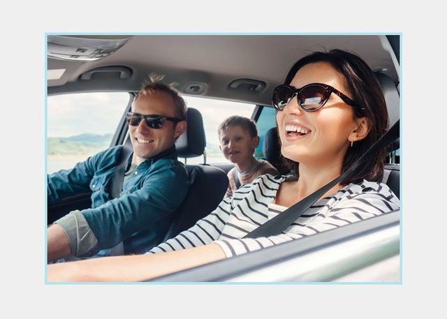 Tres pasajeros sonrientes en un coche, con gafas de sol, en un paseo soleado.