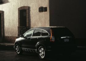 Un SUV negro estacionado junto a un edificio beige por la noche.