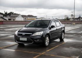 Sedán negro estacionado en una azotea mojada bajo un cielo nublado.