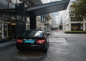 Un sedán negro estacionado bajo una moderna pasarela cubierta en un patio de la ciudad.