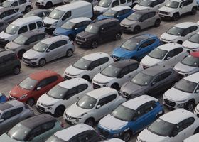 Estacionamiento abarrotado lleno de filas de autos, en su mayoría blancos, grises y negros, con algunos vehículos azules y rojos.