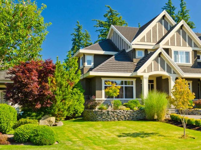 Suburban house with stone porch, manicured lawn, and colorful trees under a bright blue sky