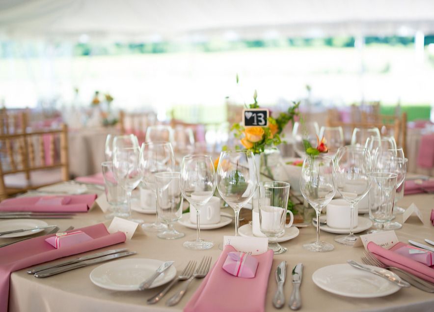 Elegant banquet table set with pink napkins, glassware, white china, and a small floral centerpiece.