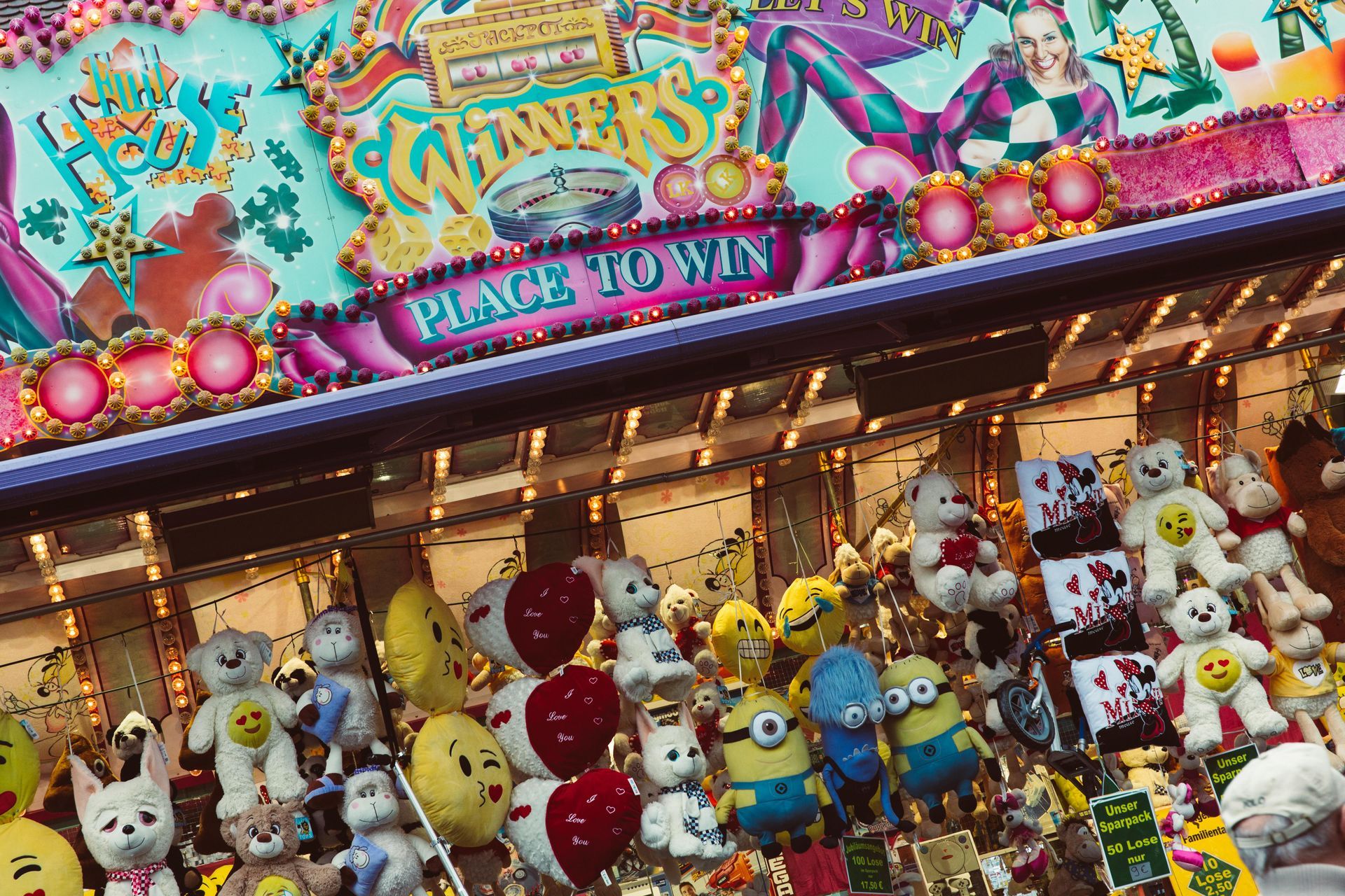 Colorful carnival prize booth filled with stuffed animals and Minions, with a “PLACE TO WIN” sign above