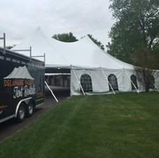 Large white event tent on a grassy slope beside a black food trailer under an overcast sky.