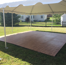 White tent canopy over a wooden dance floor on a grassy backyard lawn