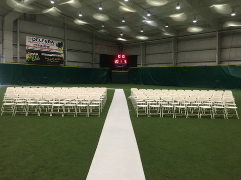 Indoor event hall with rows of white chairs facing a central aisle and a scoreboard at the far end