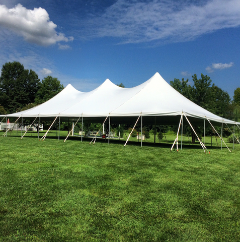 Large white event tent on a grassy field under a blue sky with clouds