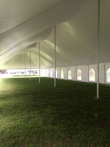 Interior of a white event tent with grass flooring and rows of arched windows along the side.