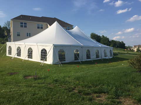 White event tent on a grassy lawn beside a beige building under a clear blue sky