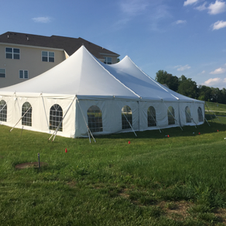 White event tent on a grassy lawn beside a beige building under a blue sky