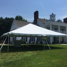 White event tent on a lawn in front of a large white house on a sunny day