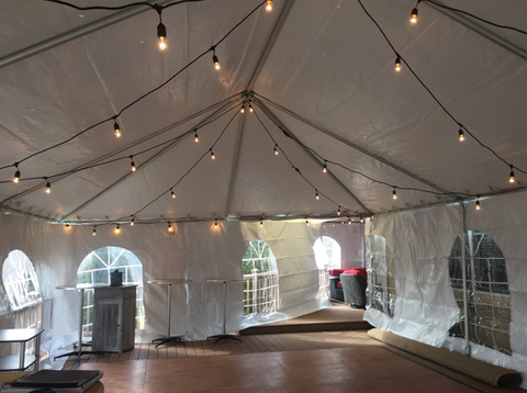 White event tent with hanging string lights and windows, mostly empty with a wooden floor.