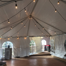Interior of a clear tent with string lights and arched windows over a wooden floor