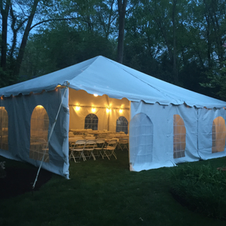 White event tent lit at dusk in a wooded outdoor setting