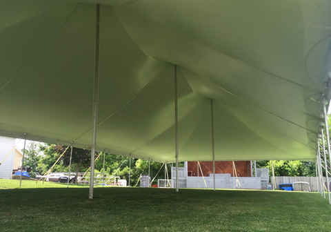 Large white event tent on a grassy lawn with metal poles and buildings in the background