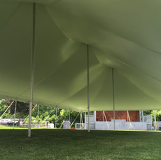 Large green tent canopy over a grassy lawn with metal poles, beside a building and trees.