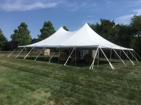 Large white event tent on a grassy field under a blue sky, with trees in the background