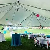 Large white event tent with teal and pink decorations, tables, and chairs on a grassy lawn