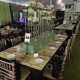 Long banquet table with green glassware, white plates, floral decor, and table number 35 in a dim hall