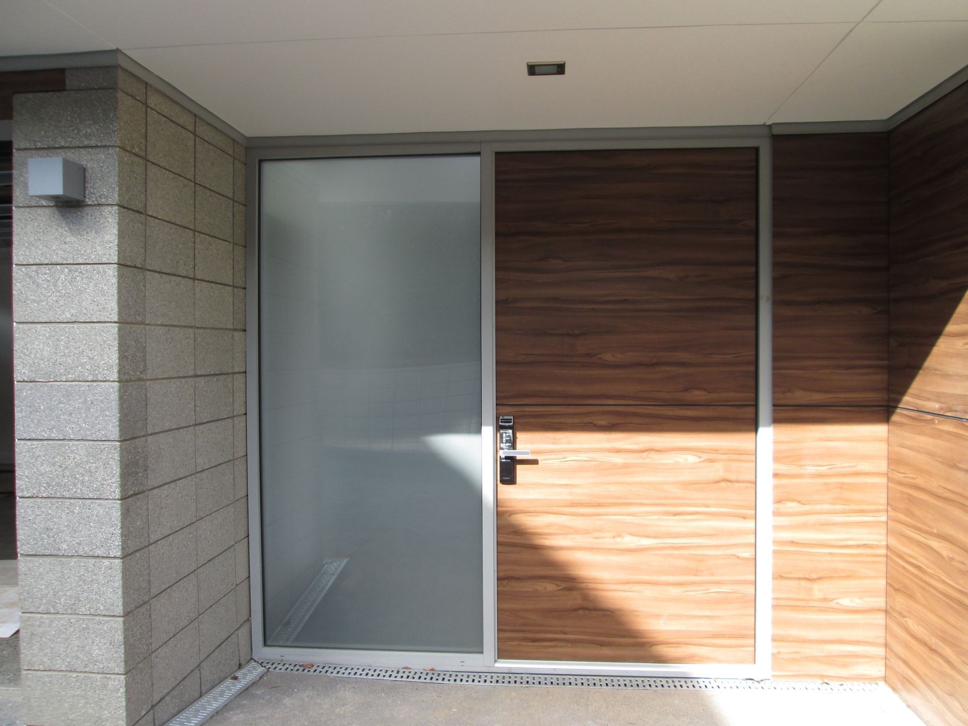 Exterior door with frosted glass panel and wood-grain section, set in a stone and wood-paneled entrance.