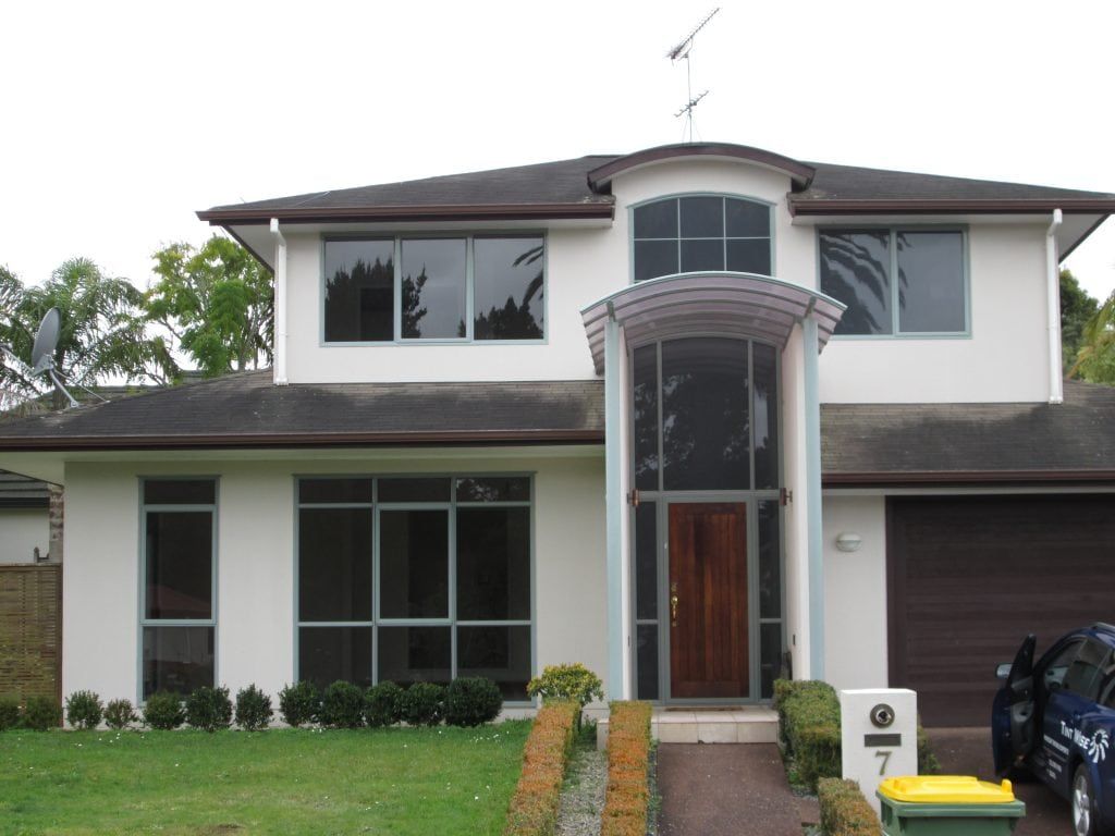 Two-story white house with dark roof and trim. Large windows, arched entryway, and a brown garage door.