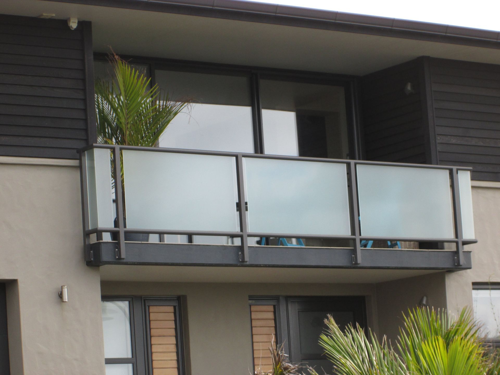 Balcony with frosted glass panels, black railing, and palm tree.