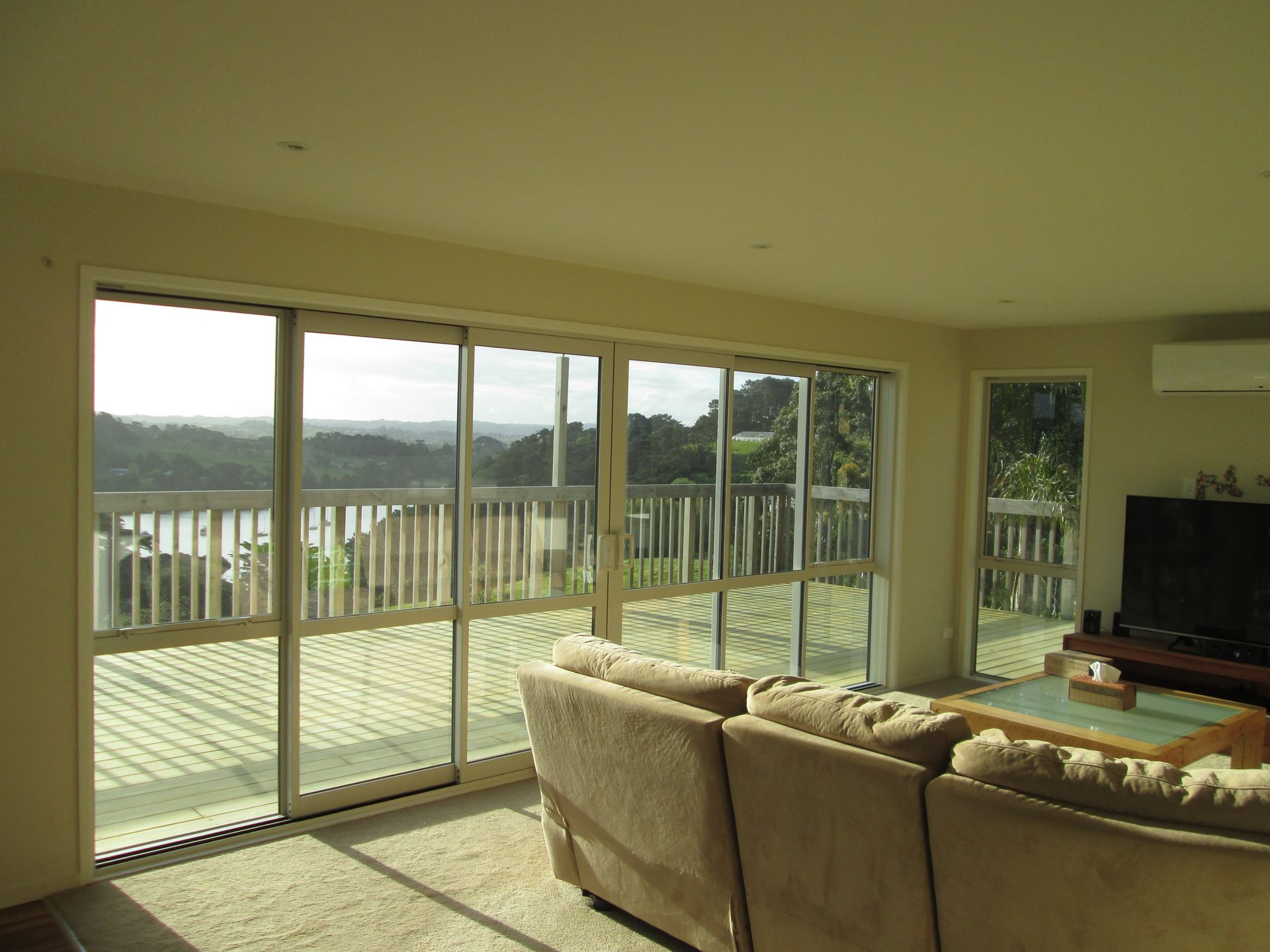 Living room with large sliding glass doors overlooking a deck and scenic view. Beige couch in the foreground.