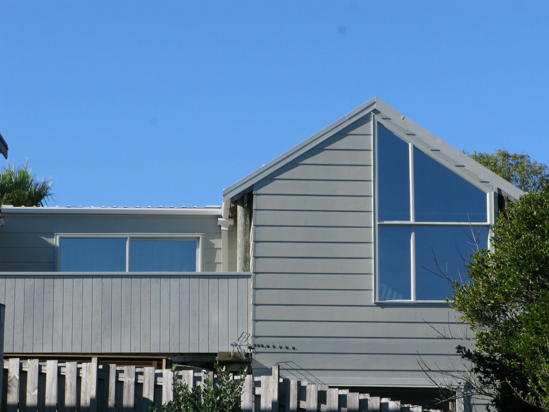 Gray house with large triangular window and a wooden fence.