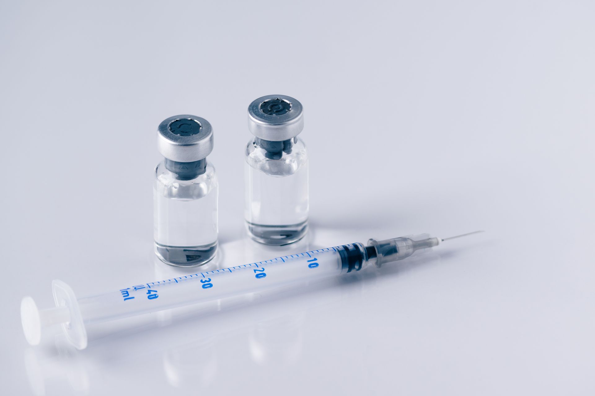 A syringe and two bottles of liquid on a white surface.