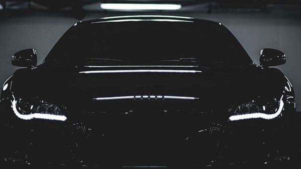 Front view of a black car in a dark garage, with headlights glowing softly.