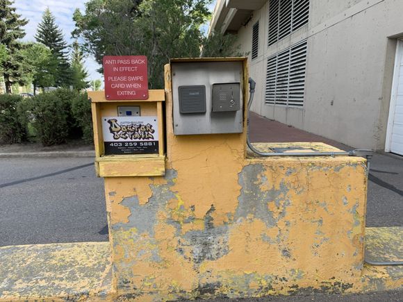 Weathered yellow utility wall with electrical boxes and a red warning sign beside a building walkway