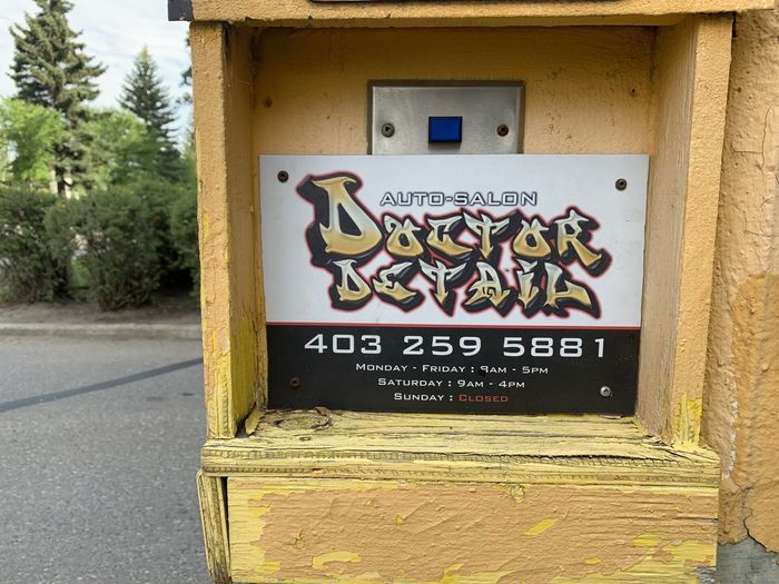 Graffiti-style sign reading “Doctor” with phone number 403-259-5881 on a yellow utility box