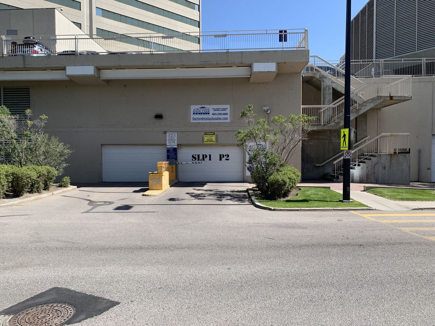 Concrete parking garage entrance with white garage door, signs, and a small tree by the curb