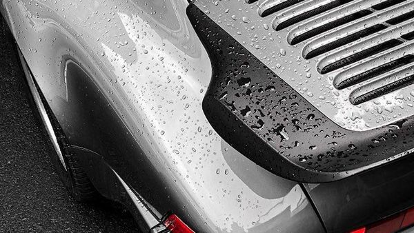 Close-up of a wet silver sports car rear with black vent and raindrops