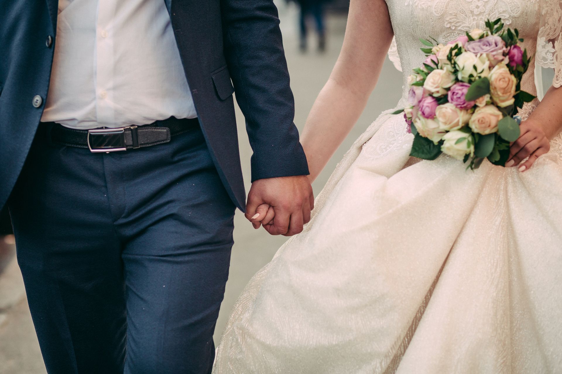 A bride and groom are holding hands while walking down the street.