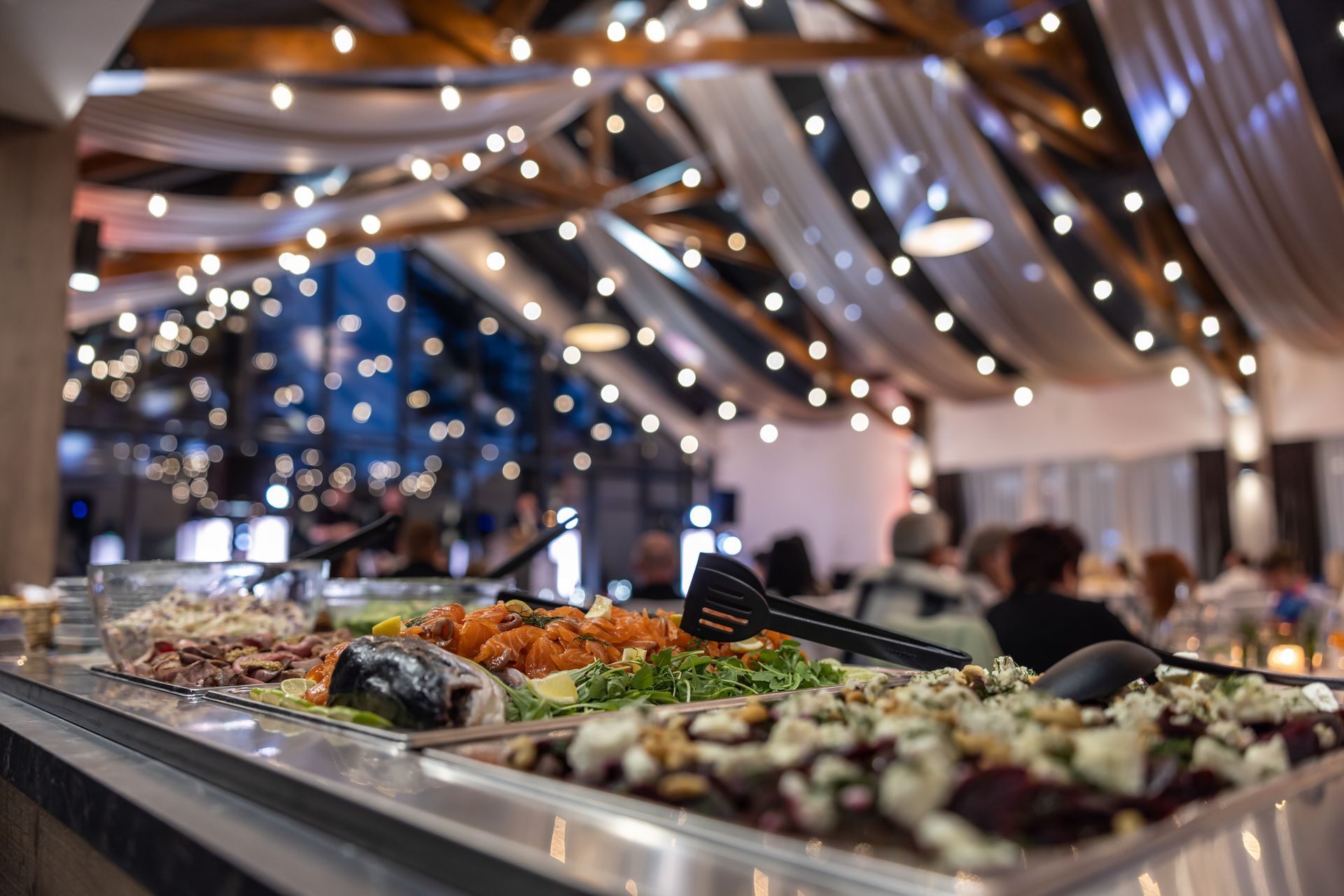 A buffet table with lots of food and tongs in a restaurant.