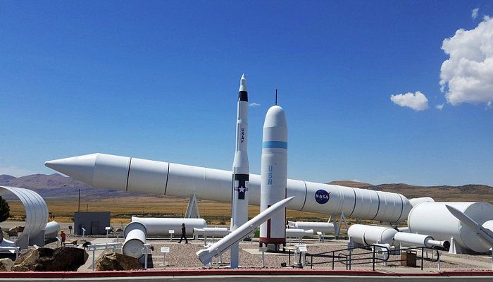 White rocket displays and spacecraft parts arranged in an outdoor desert museum under a clear blue sky.