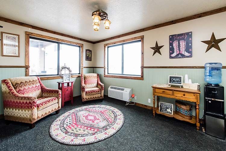 A waiting area with two patterned armchairs, a wooden console table, a water cooler, and country-themed decor.