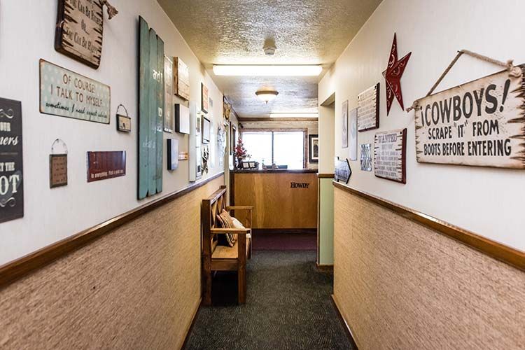 A narrow hallway with a wood bench, beige wallpaper, and various rustic signs decorating the white walls.