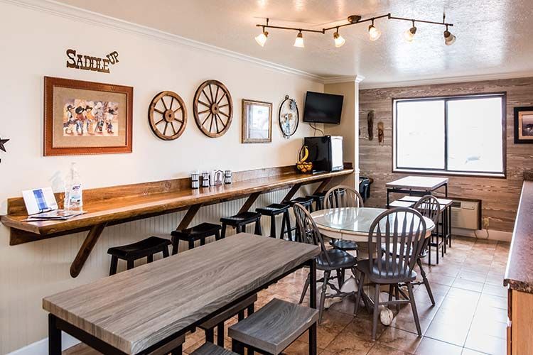Western-themed dining area with a long wooden counter, stools, and tables against a light wall decorated with wheels.
