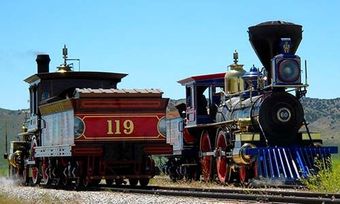 Two historic steam locomotives, one numbered 119, side by side on tracks against a clear blue sky.