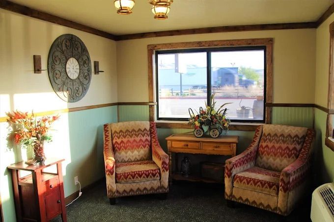 Two patterned armchairs and a wooden side table sit near a window in a room with light green walls and wood trim.