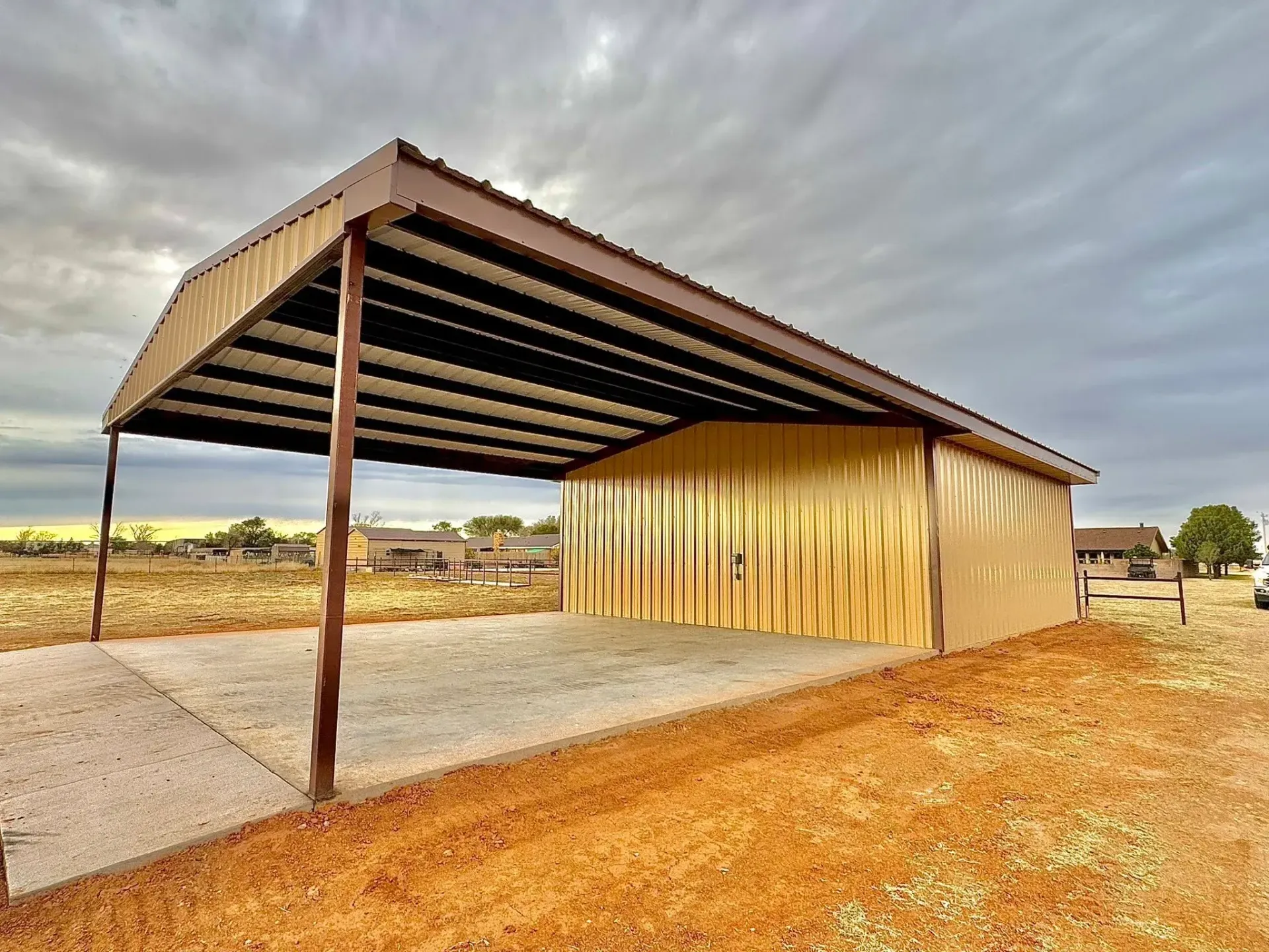 Open-sided metal shed in a dry rural field under a cloudy sky