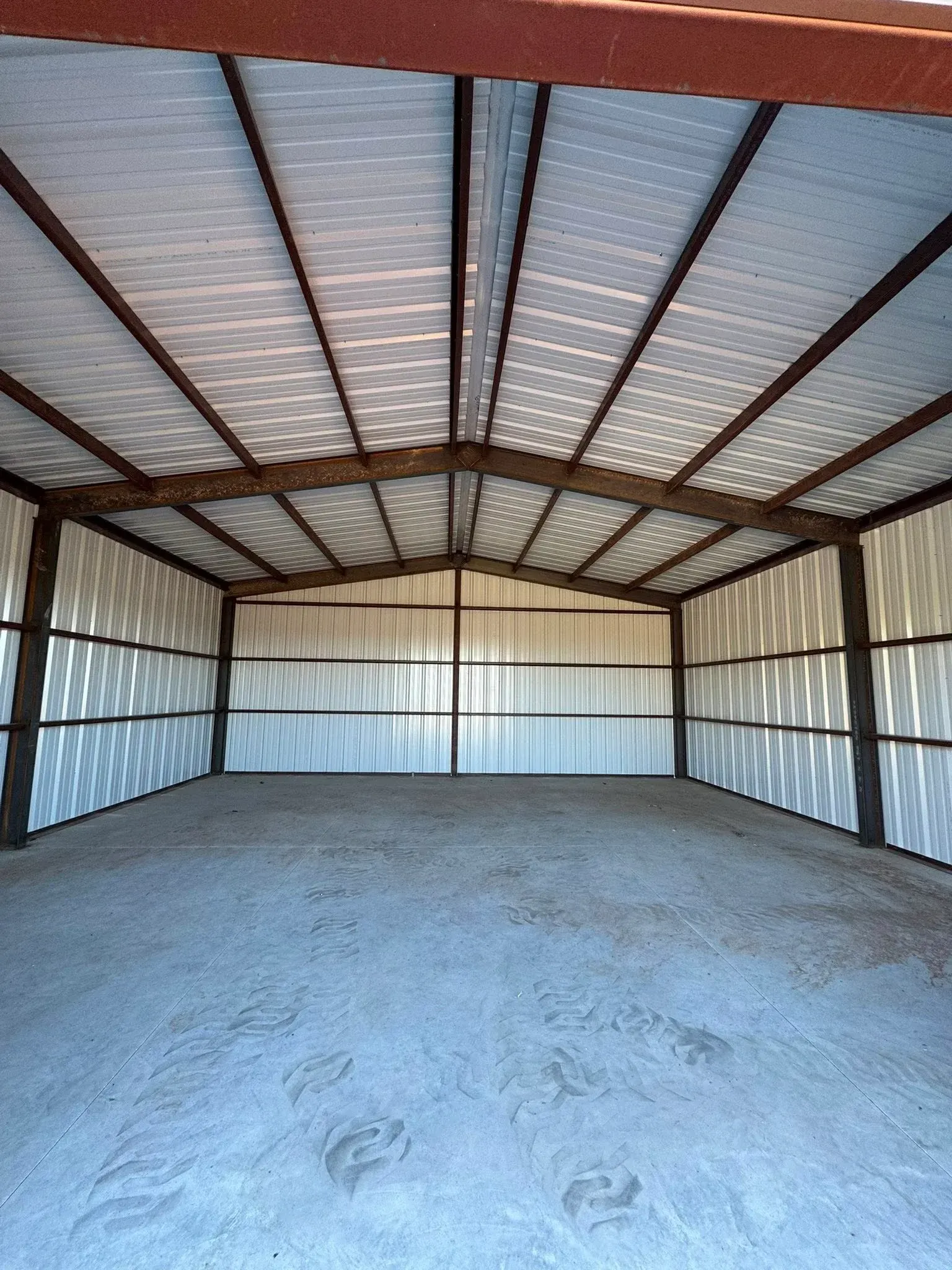 Empty metal storage shed with corrugated walls, exposed beams, and a concrete floor.