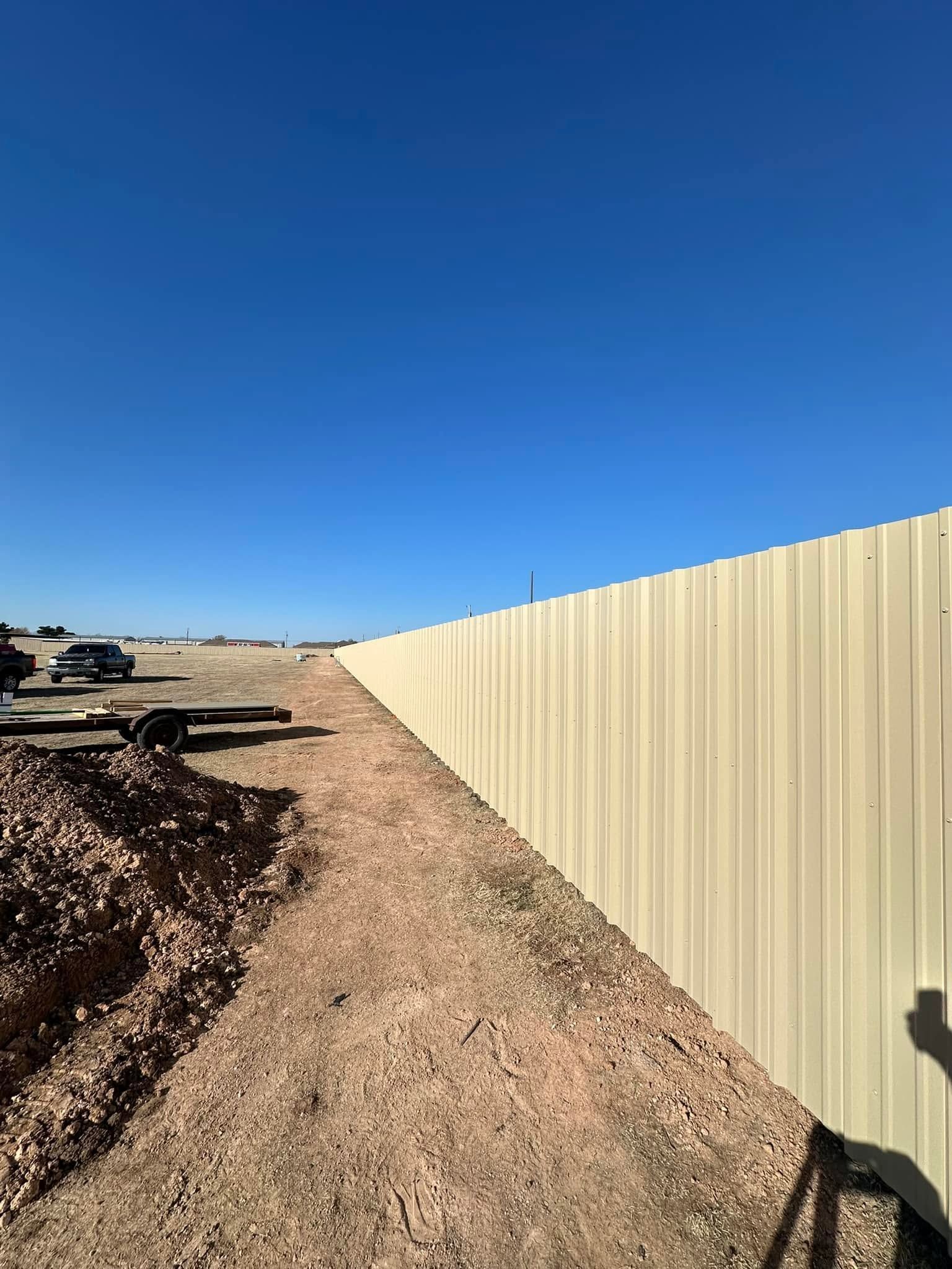 Gravel path beside a beige corrugated fence under a clear blue sky