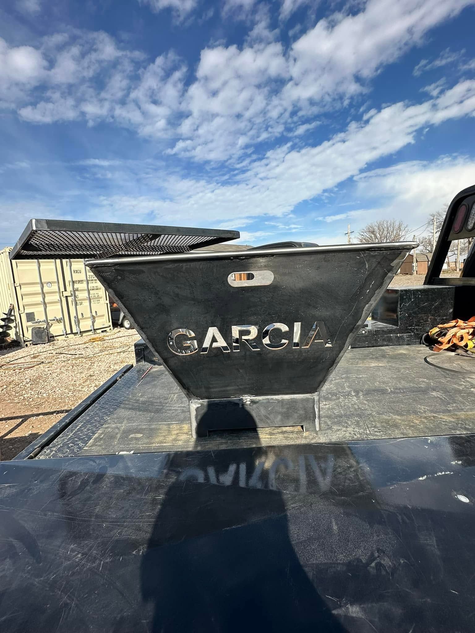 Black GARCIA dumpster on a construction site under a cloudy blue sky.