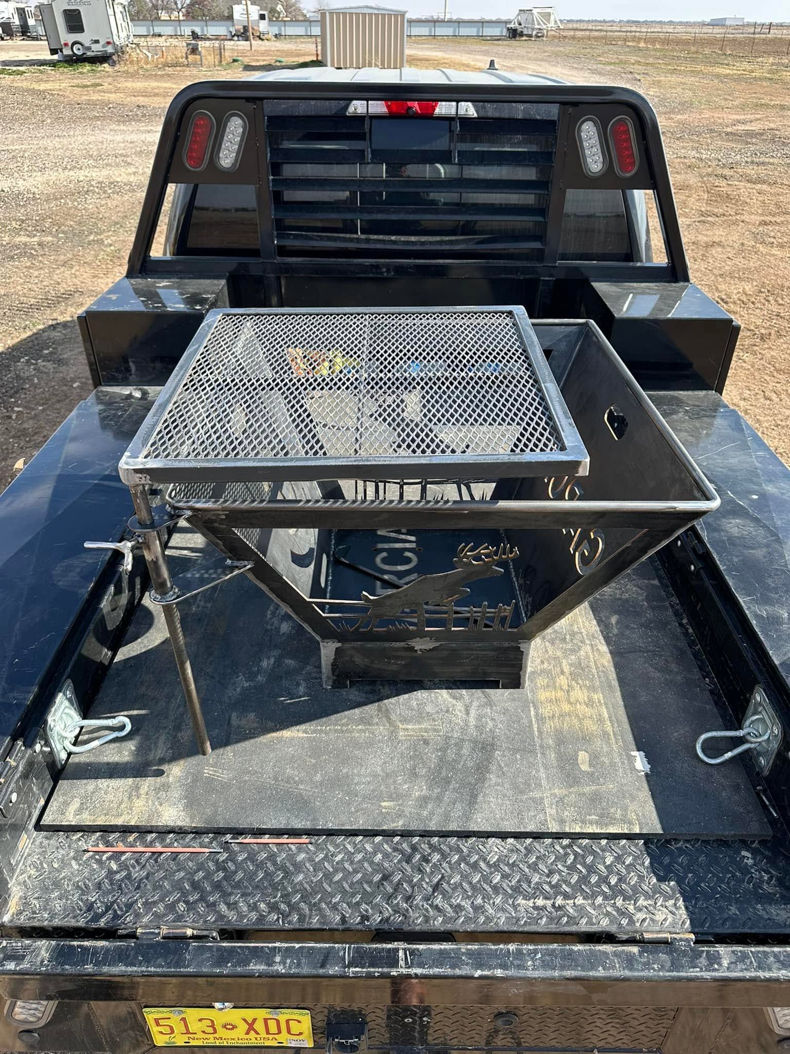 Black utility trailer with a front-mounted diamond-plate grill and storage rack in a gravel lot