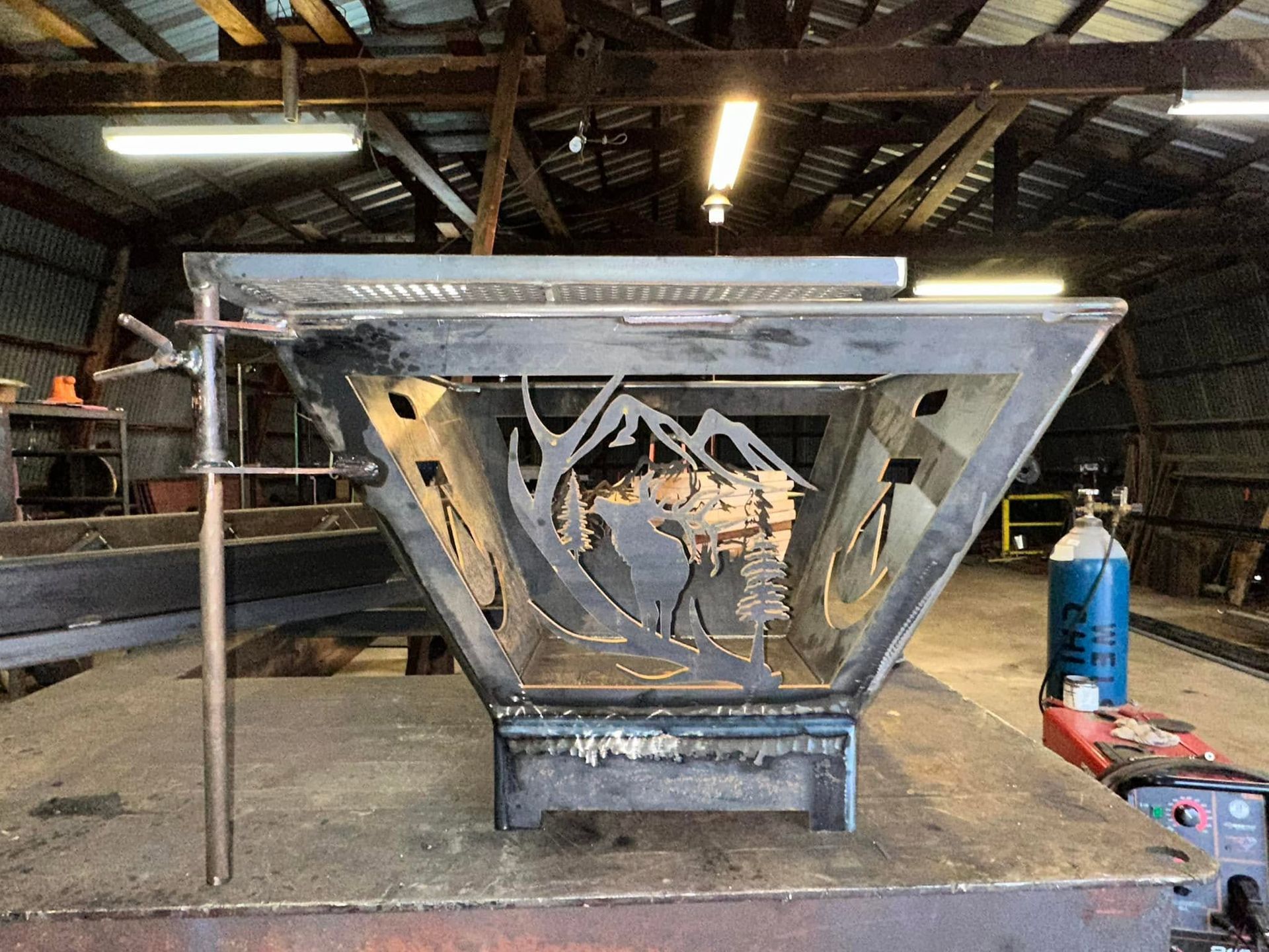 Worn metal industrial structure in a workshop, with triangular supports and a blue gas cylinder nearby.